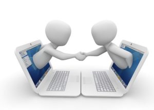 Two people coming out of computers and shaking hands